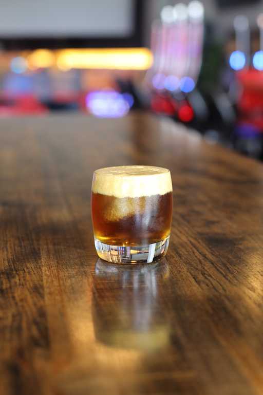 "Maple Old Fashioned" cocktail at Jive Lounge, a rich and smooth whiskey-based drink with a hint of maple, served over ice in a short glass on a wooden table.