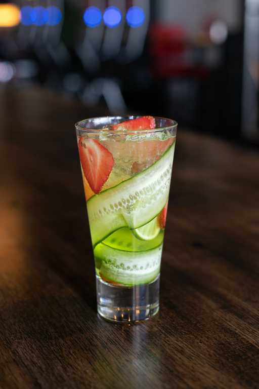 "Summer Day" cocktail at Jive Lounge, a refreshing drink infused with cucumber and strawberry slices, served over ice in a tall glass on a wooden table.