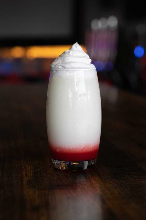 "Strawberry Swirl Colada" at Jive Lounge, a creamy tropical cocktail with a vibrant strawberry base, topped with fluffy whipped cream, served in a tall glass.