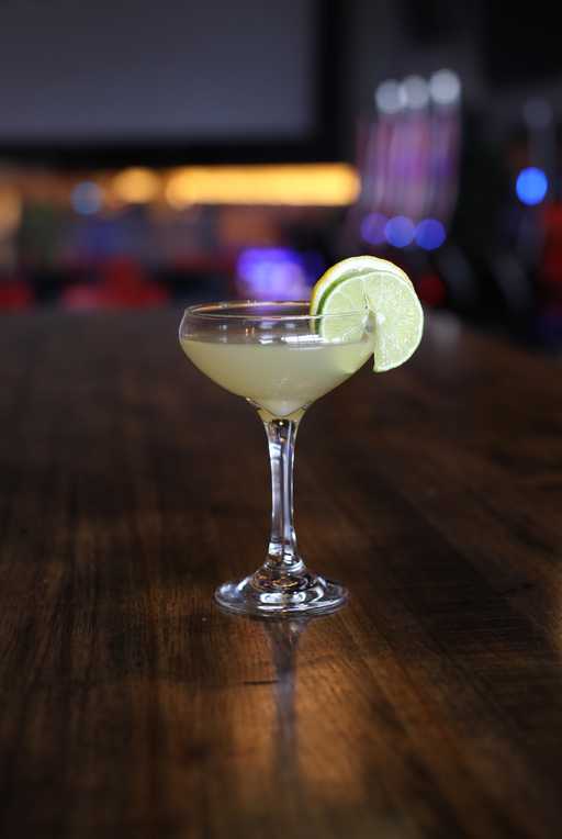 "Paris Is Burning" cocktail at Jive Lounge, a sophisticated drink served in a coupe glass, garnished with a fresh lime slice on a wooden table.