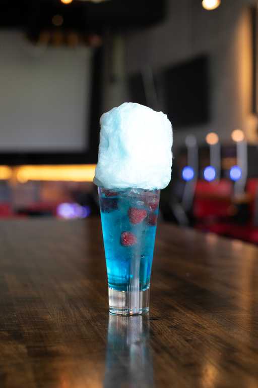 "Sweetwater Delight" cocktail at Jive Lounge, a vibrant blue drink with fresh raspberries, topped with fluffy blue cotton candy, served in a tall glass.